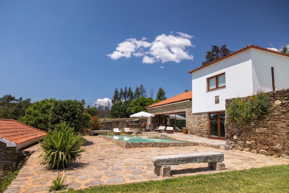 Portuguese stone house with a pool, patio and lush garden on a sunny day
