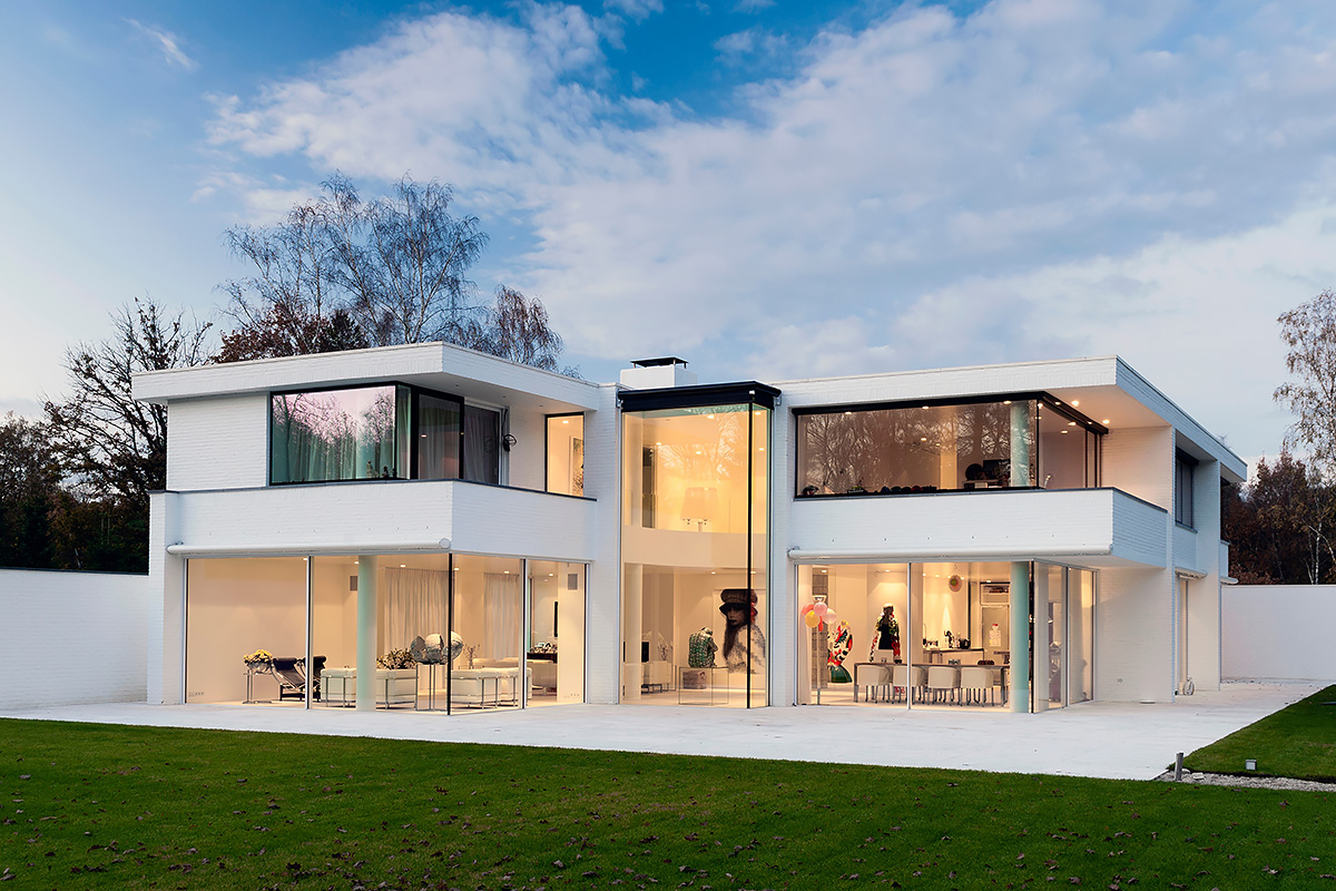 Large white minimalist villa with expansive glass windows and manicured lawn