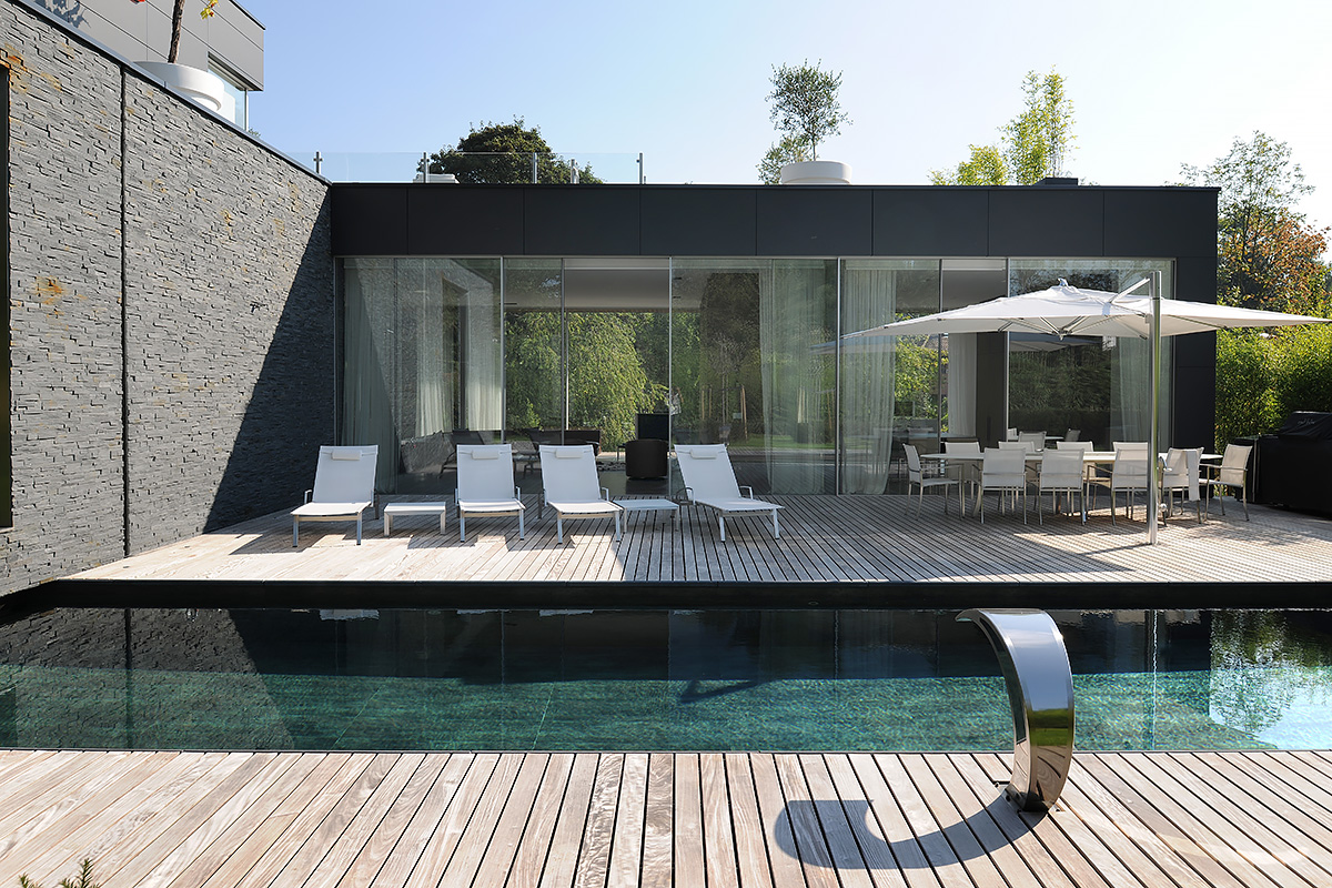 Backyard design featuring stone wall, wooden pool deck, and white loungers