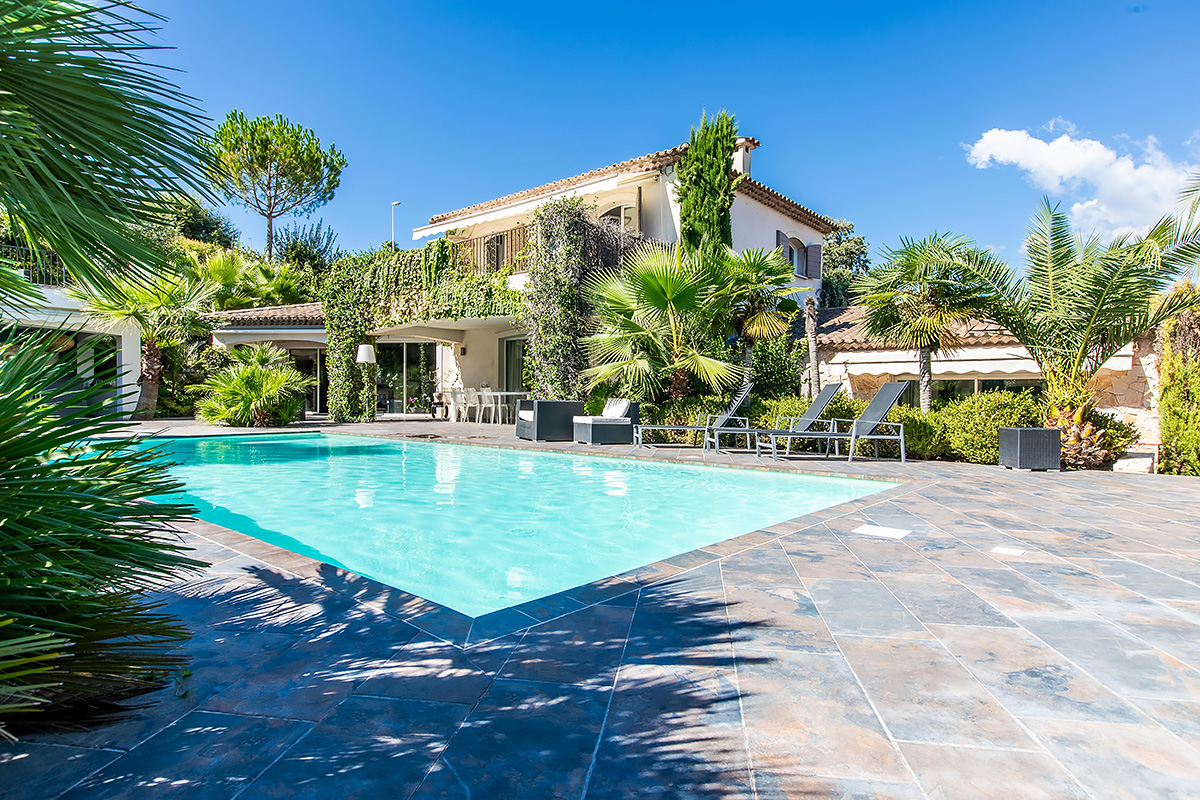 Mediterranean-style luxury villa with turquoise pool, stone patio, and palm trees