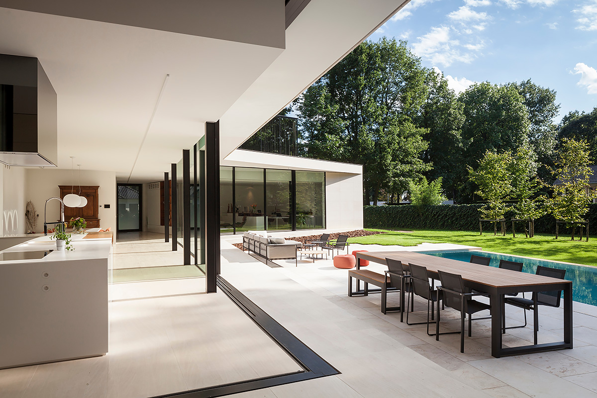 Modern open-plan kitchen and patio with long dining table, outdoor pool and garden
