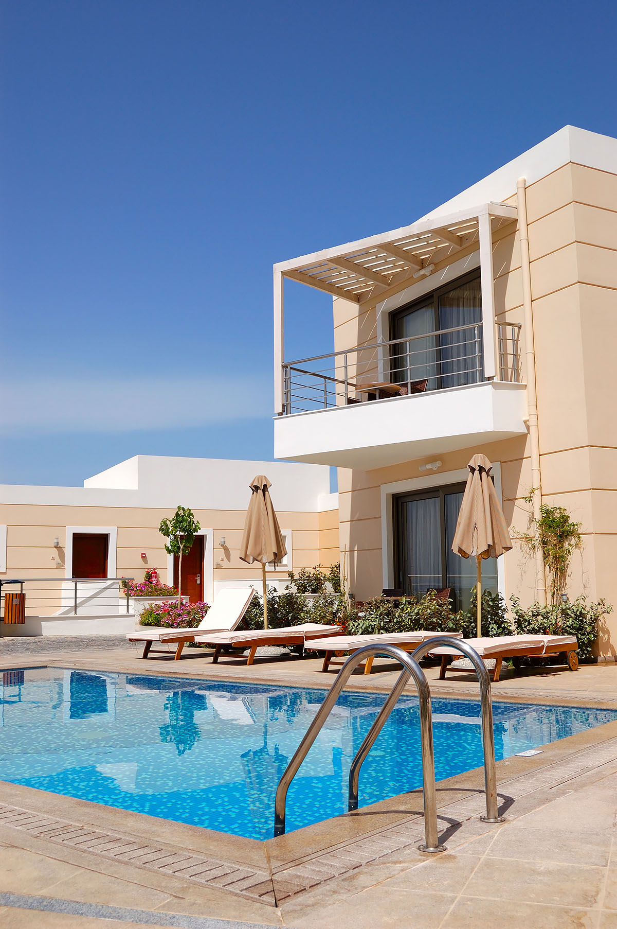 Luxury resort pool with sun loungers and modern balcony under a clear blue sky