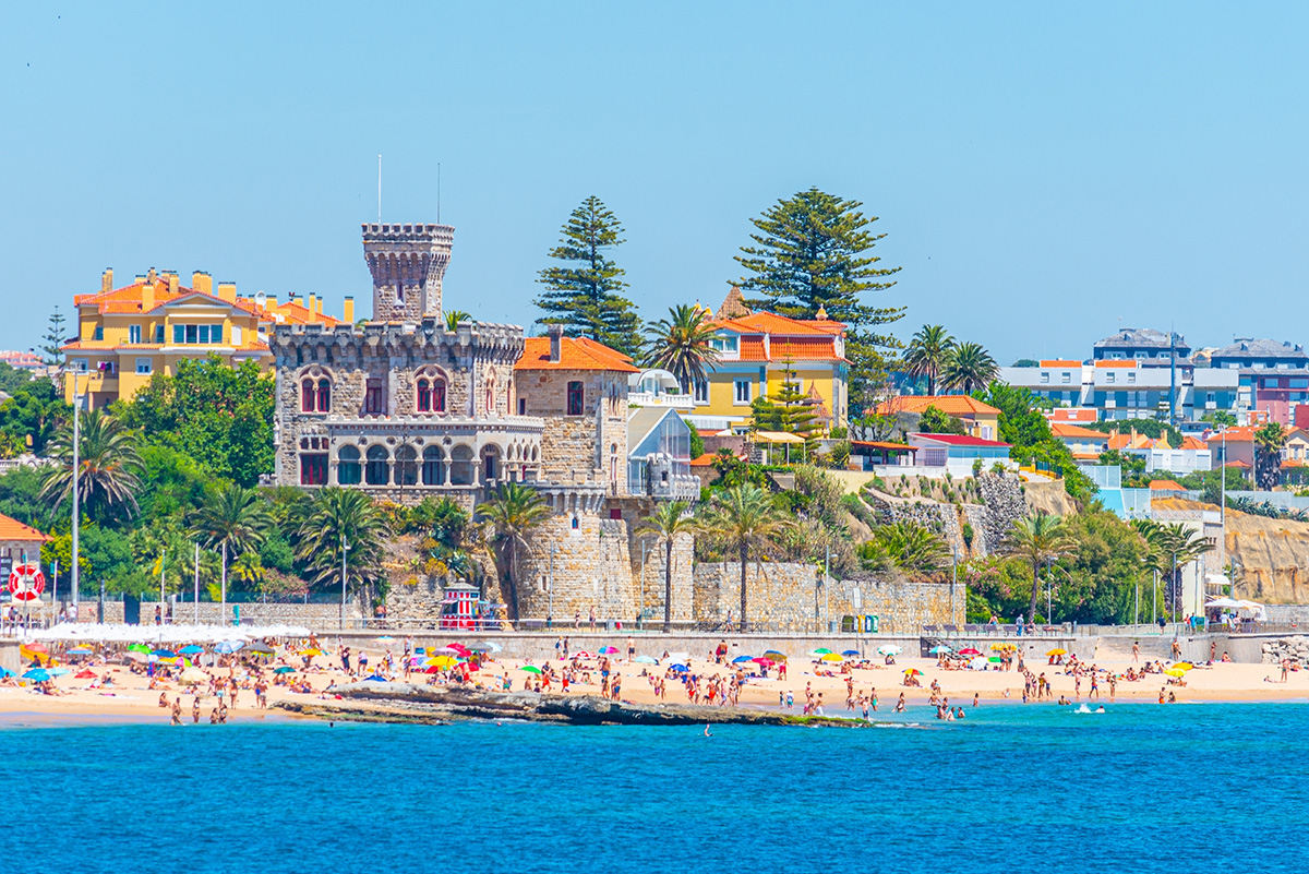 Crowded beach in Estoril, Portugal, featuring the historic Forte da Cruz by the sea