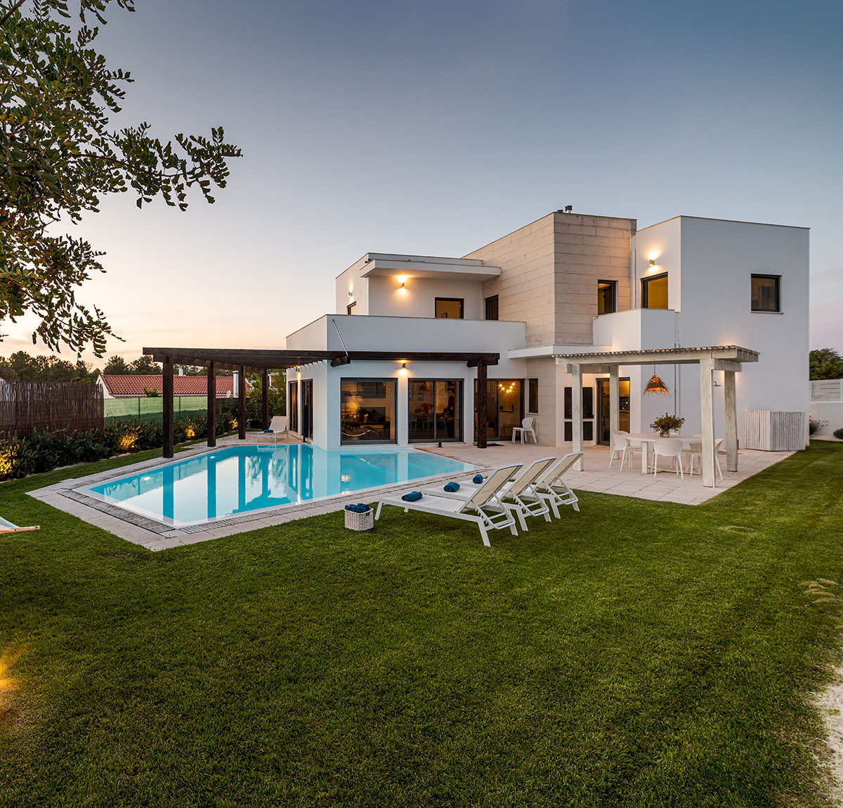 Luxury vacation home with backyard pool, green lawn, and hammock at sunset