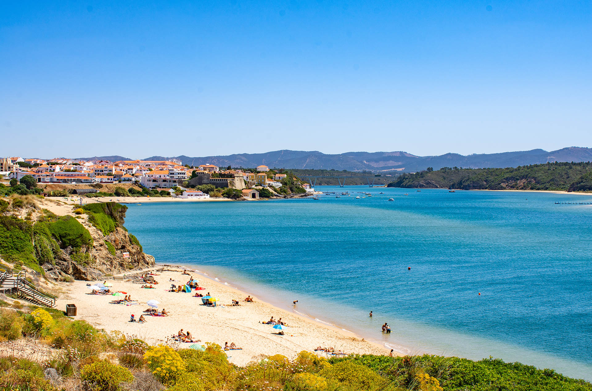 Sunny beach at Vila Nova de Milfontes, Portugal, with blue water and white buildings