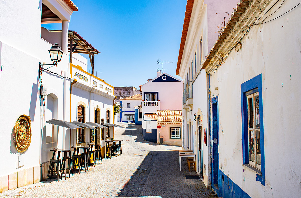 Bright street in Vila Nova de Milfontes, Portugal, with white buildings and blue trim
