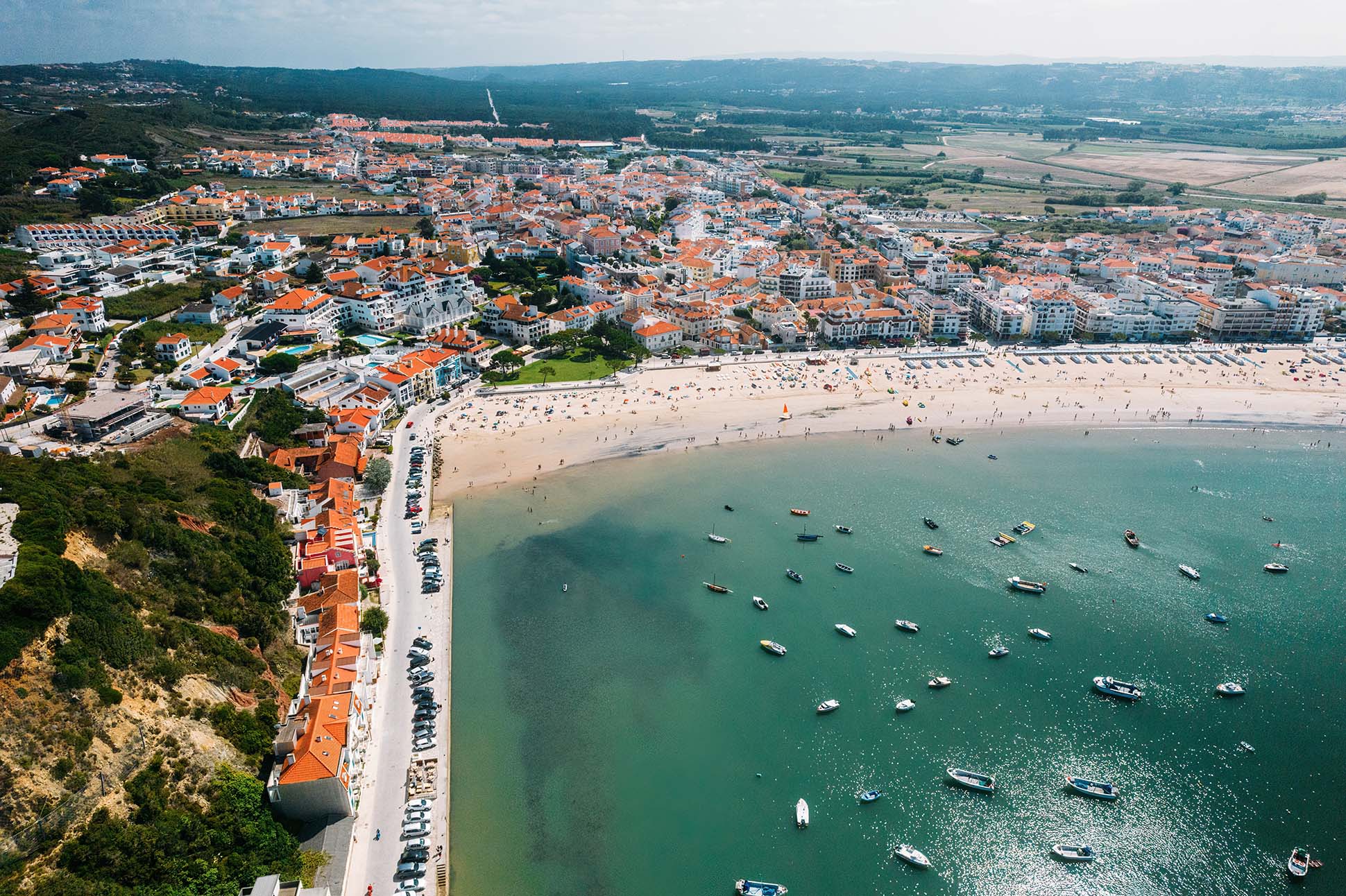 Panoramic view of São Martinho do Porto bay with parked boats, red-tiled roofs and green cliffs