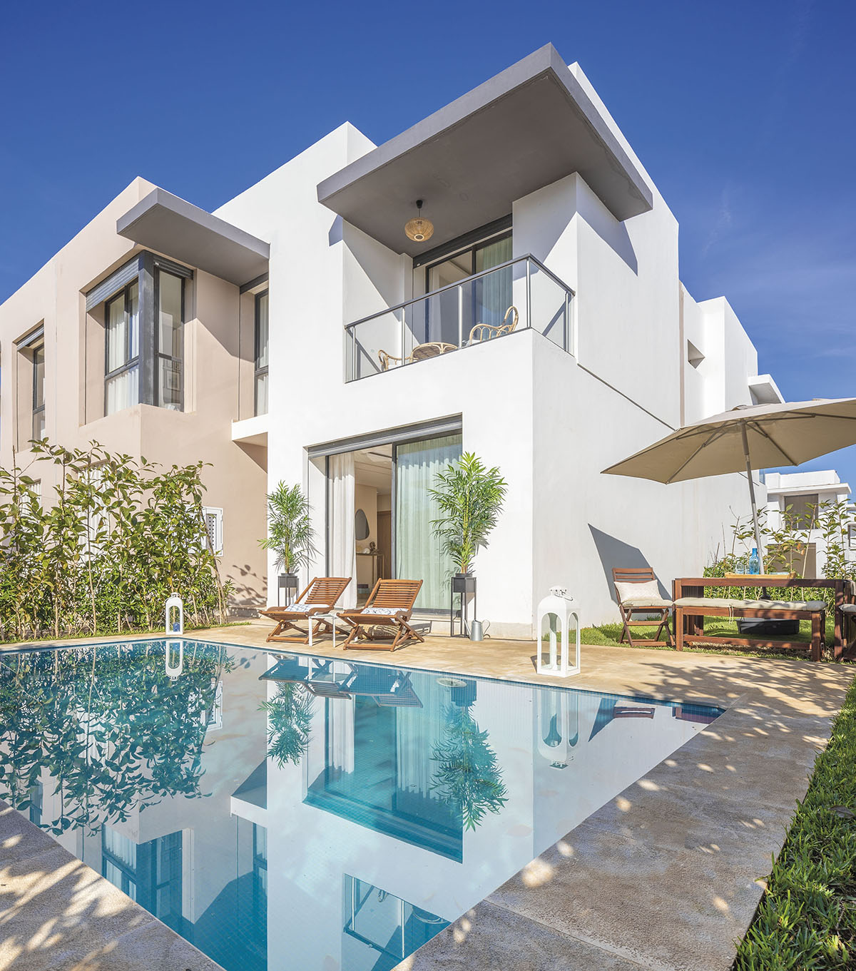 Modern white villa with a private swimming pool, wooden lounge chairs and garden