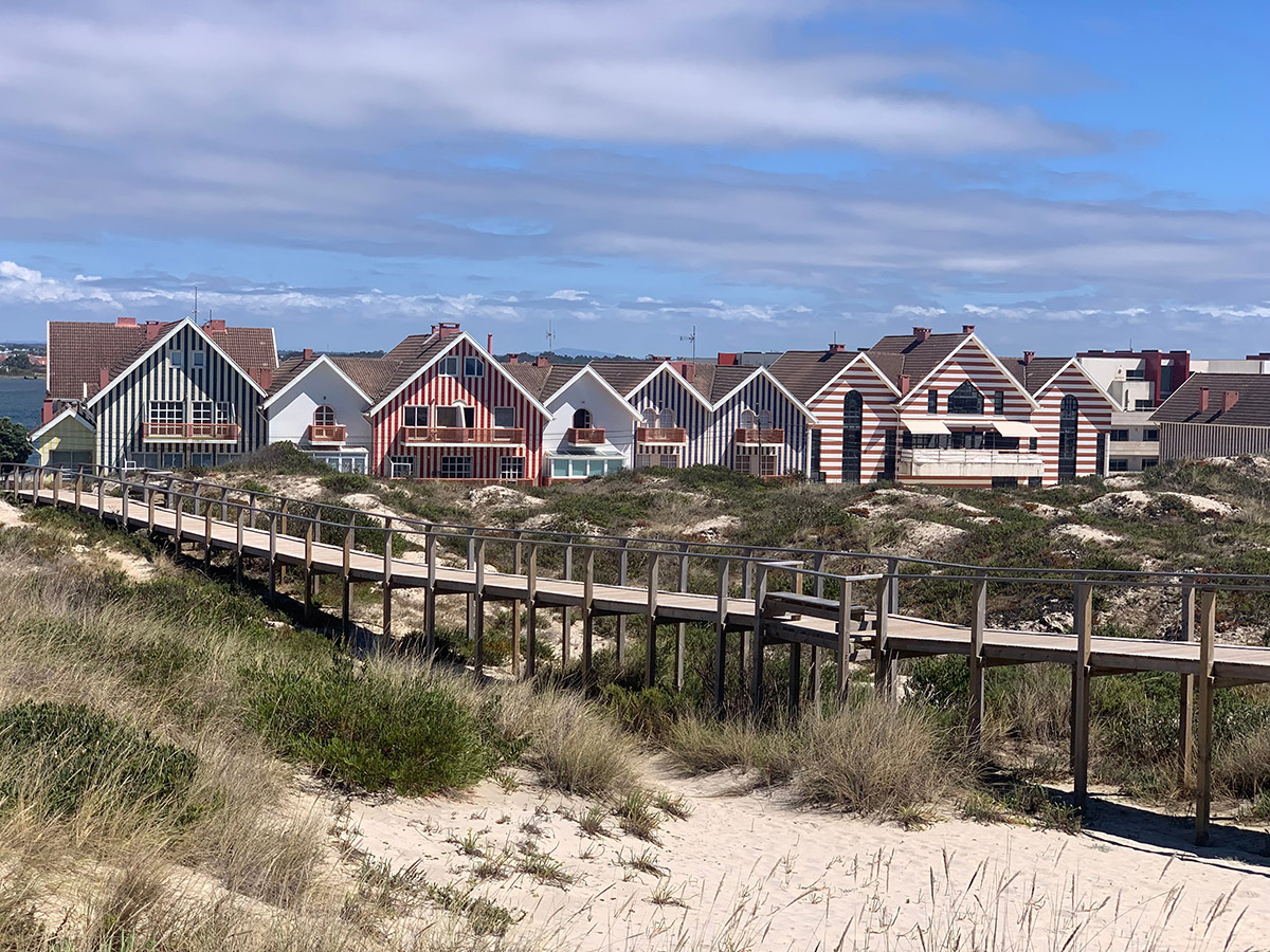 Colorful striped houses and a wooden boardwalk over sandy dunes in Costa Nova, Portugal