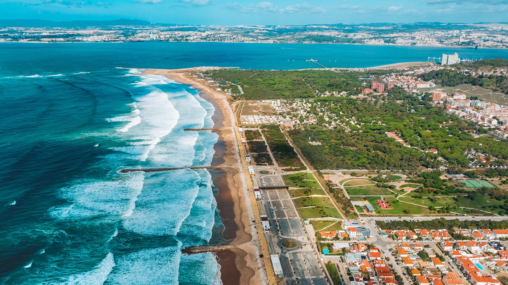 Bird's-eye view of Costa da Caparica coastline with turquoise waves and forested park
