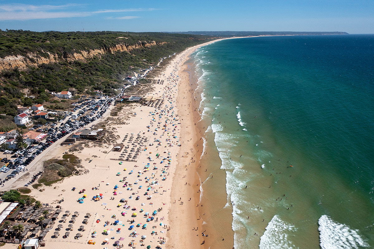 Aerial image of a crowded sandy beach lined with green cliffs and deep blue ocean