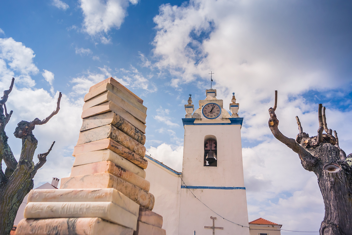 Marble book sculpture in front of the historic Igreja de São Pedro church in Melides