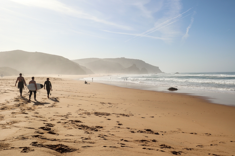 Surfers walking on vast beach in Portugal at sunrise
