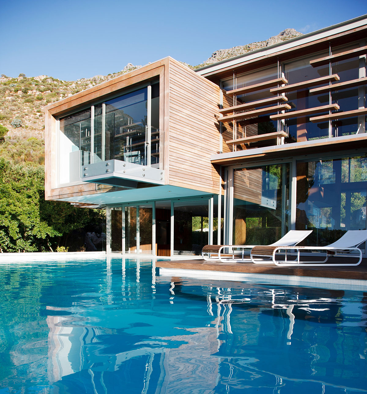 Modern wood-clad luxury villa with a cantilevered balcony overlooking a bright blue pool