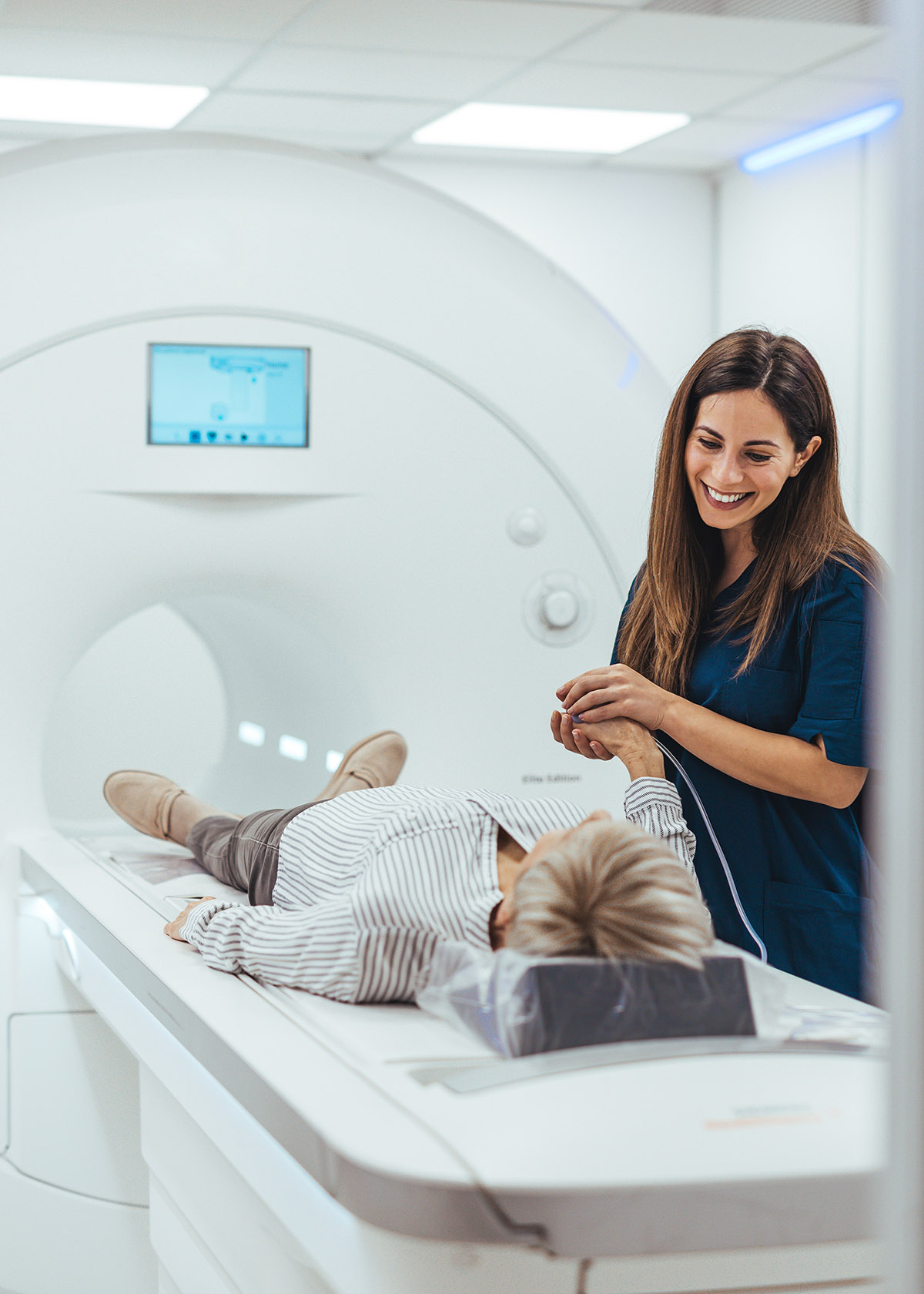Smiling medical professional comforts a patient lying on an MRI scanner bed in a clinic
