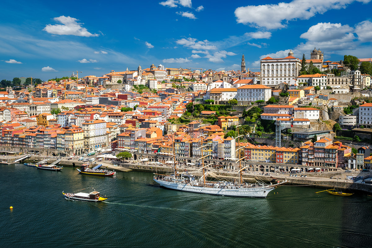 Aerial view of a white tall ship and traditional Rabelo boats on the Douro River in Porto