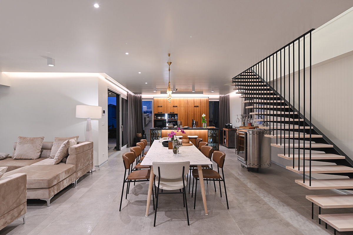 Modern open-plan living area with a marble dining table, velvet sofa, and floating staircase