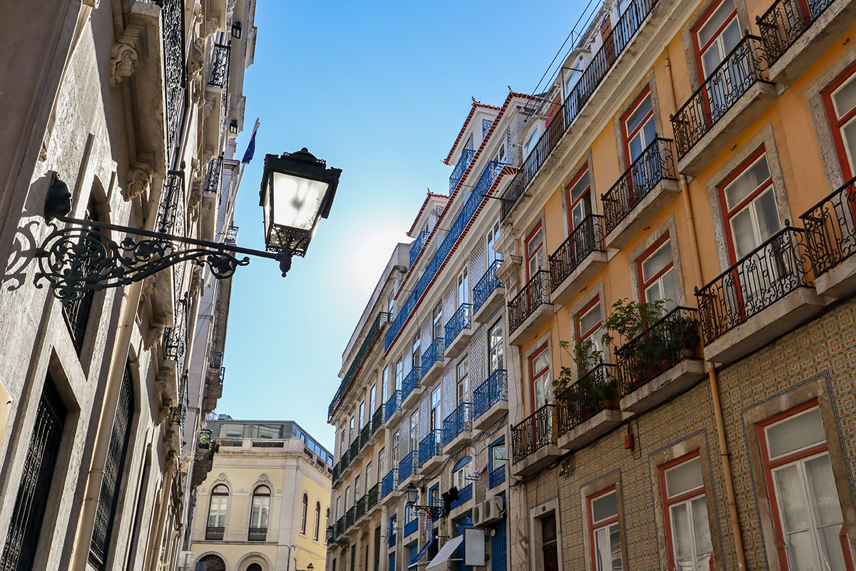 Historic wrought-iron street lamp on a narrow street with colorful tiled buildings in Lisbon