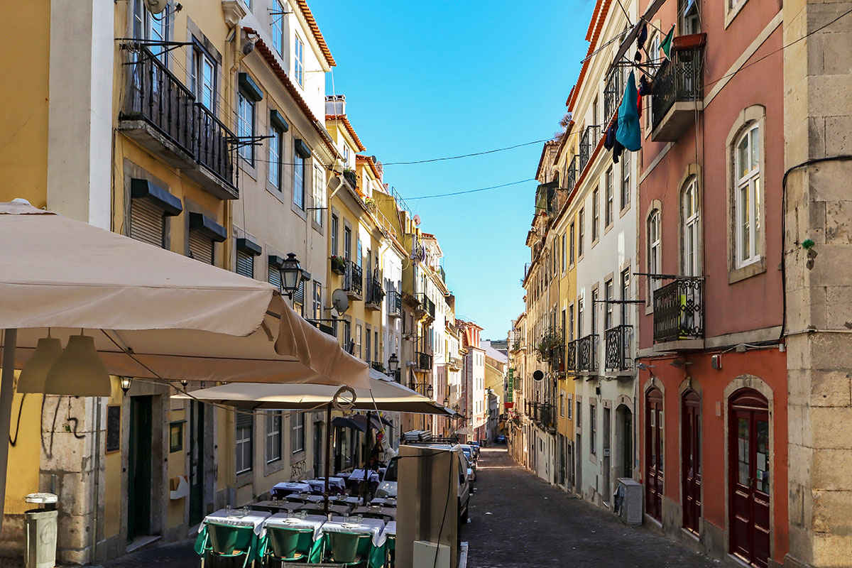 Narrow cobblestone street in Lisbon with outdoor cafe seating and colorful historic buildings