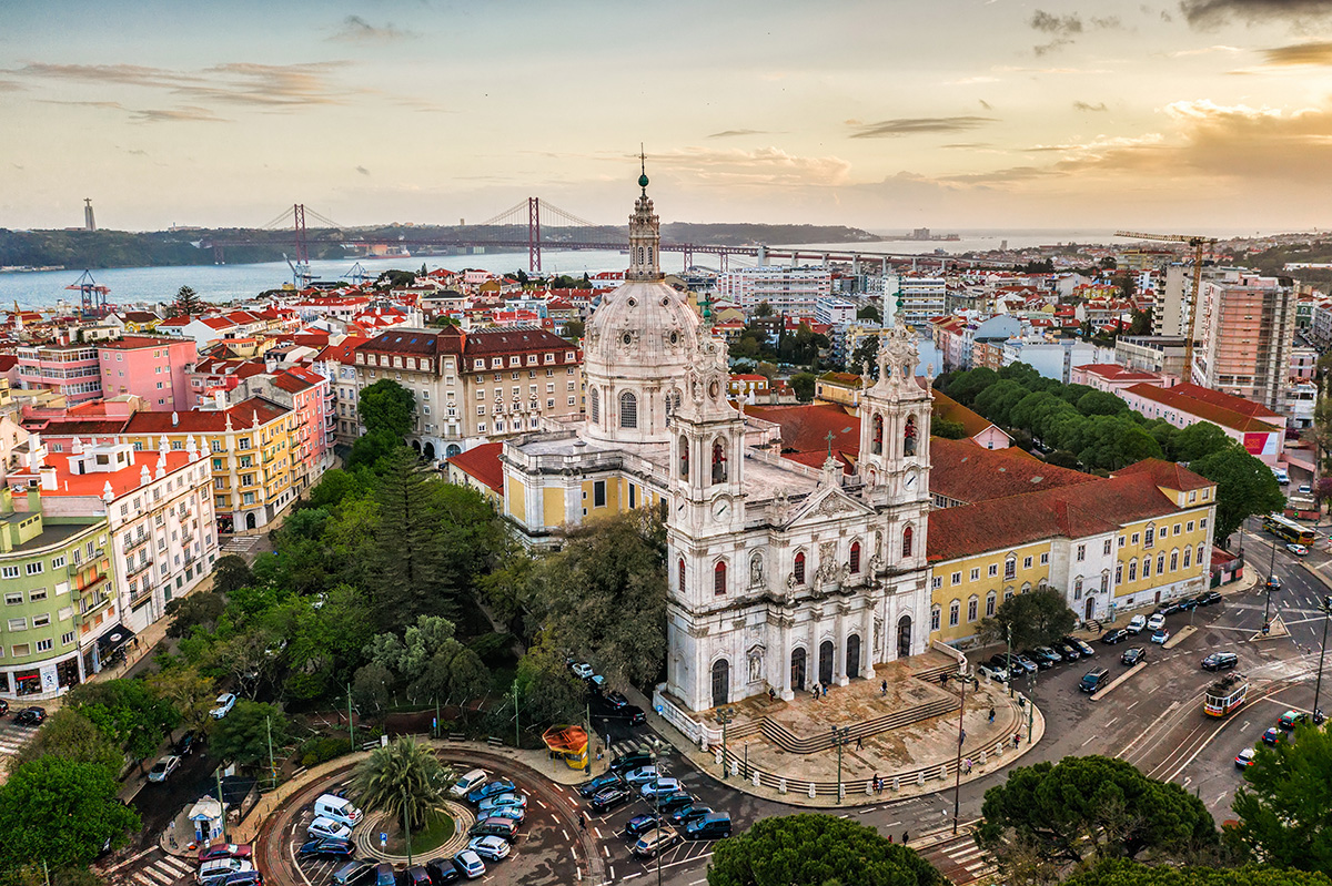 Striking view of the Estrela Basilica in Lisbon at sunset with the 25 de Abril Bridge