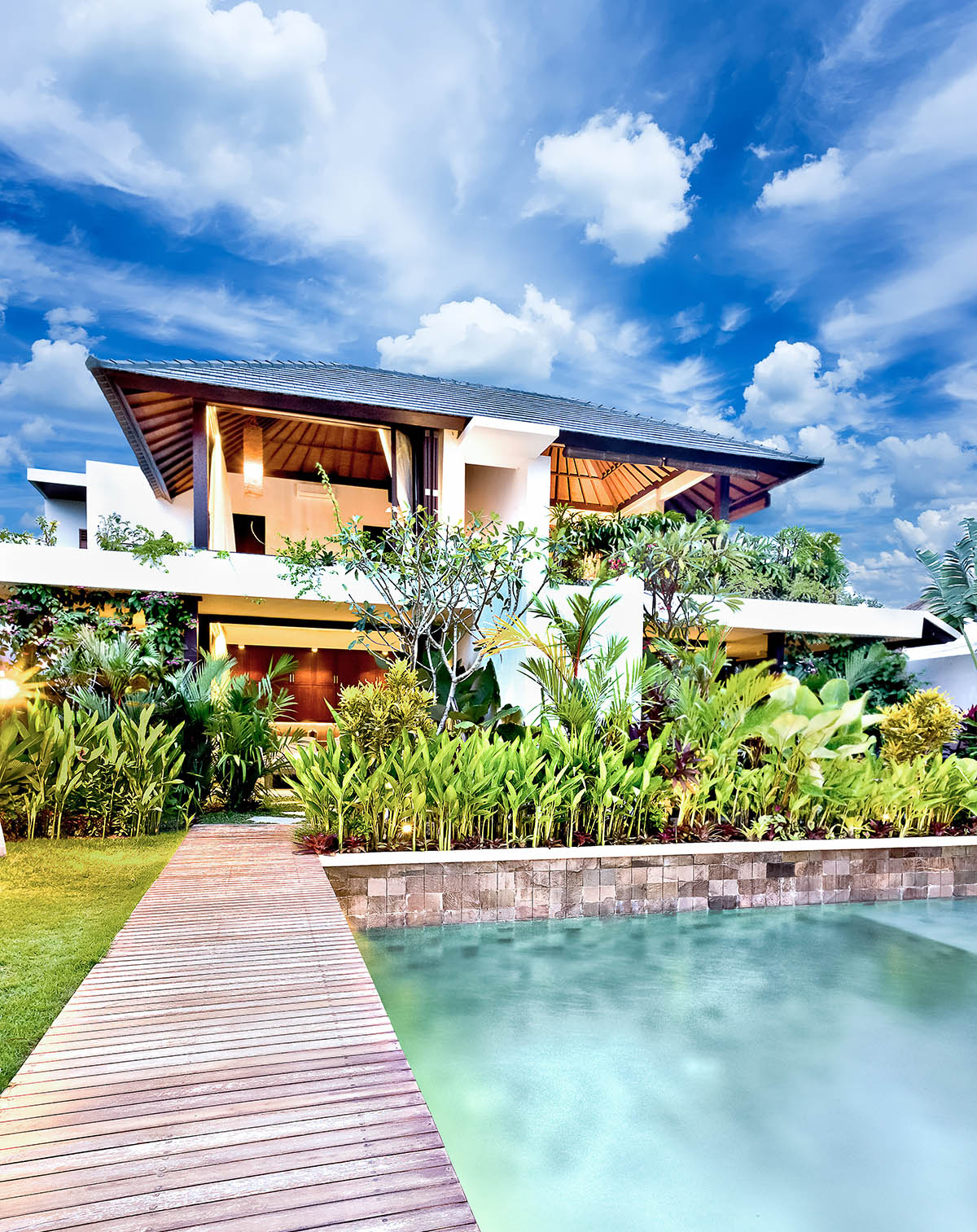 Luxury two-story tropical villa with lush gardens, a wooden walkway, and a private pool