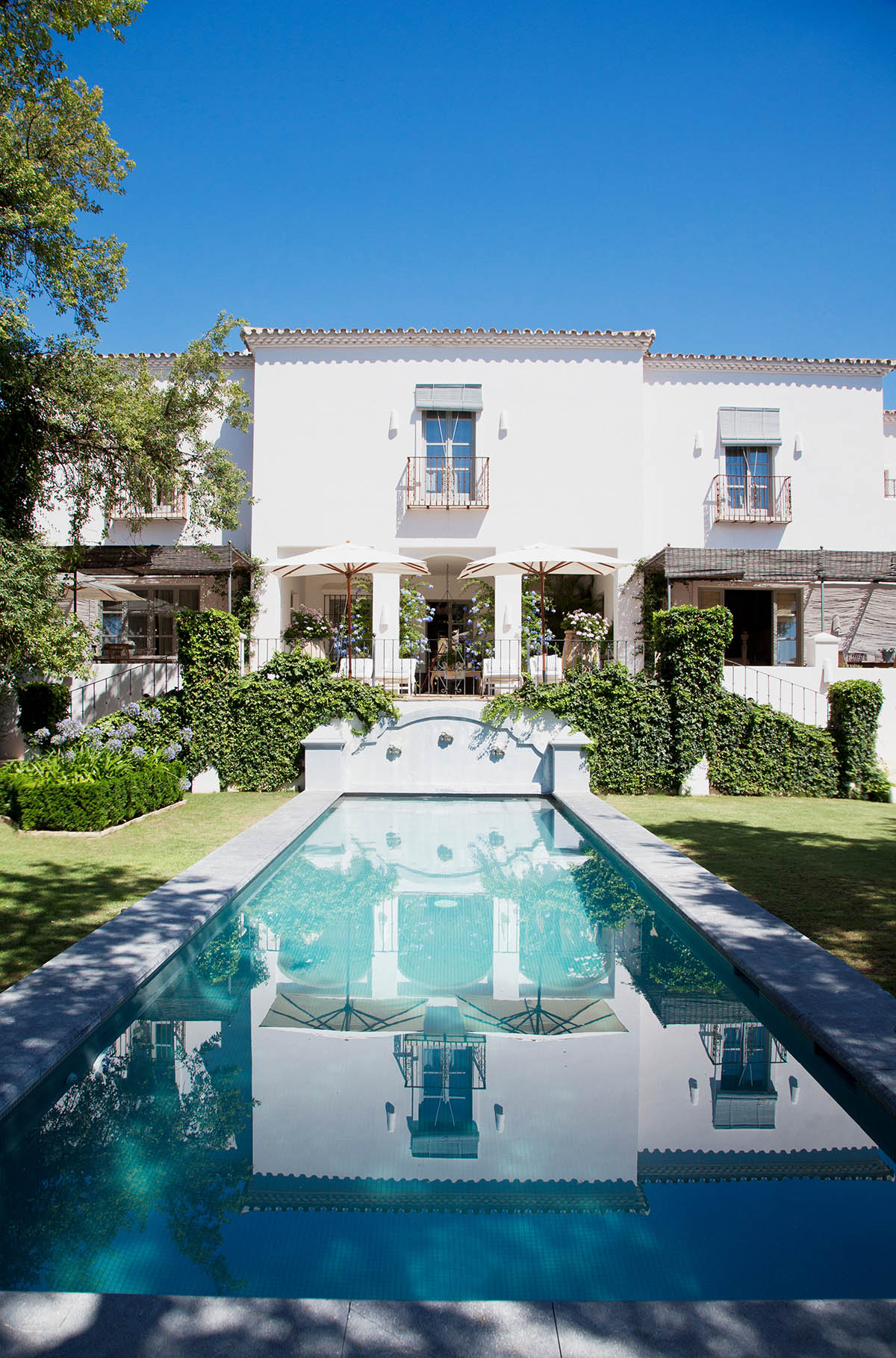 A white Mediterranean villa with a reflecting pool and symmetrical architecture