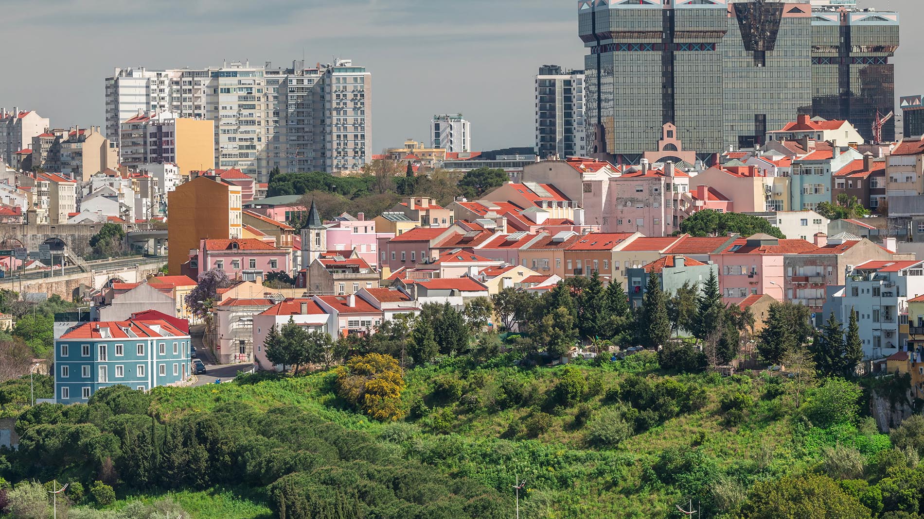 A cityscape view of Lisbon with colorful houses, green hills, and modern glass skyscrapers