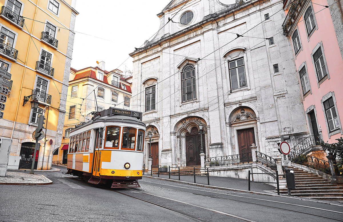 Yellow Tram 28 climbing a steep hill in front of a white church in Lisbon