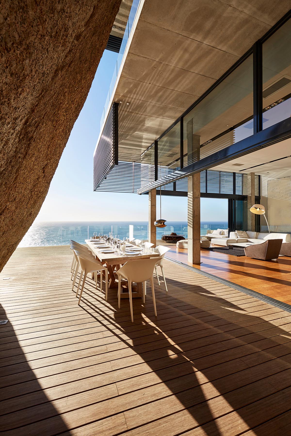 Modern terrace with wooden decking and a long dining table overlooking the ocean