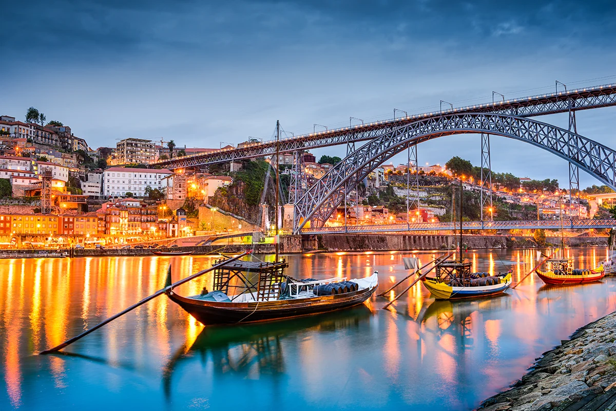 Historic Porto cityscape at night with Dom Luís I Bridge and Douro River Rabelo boats