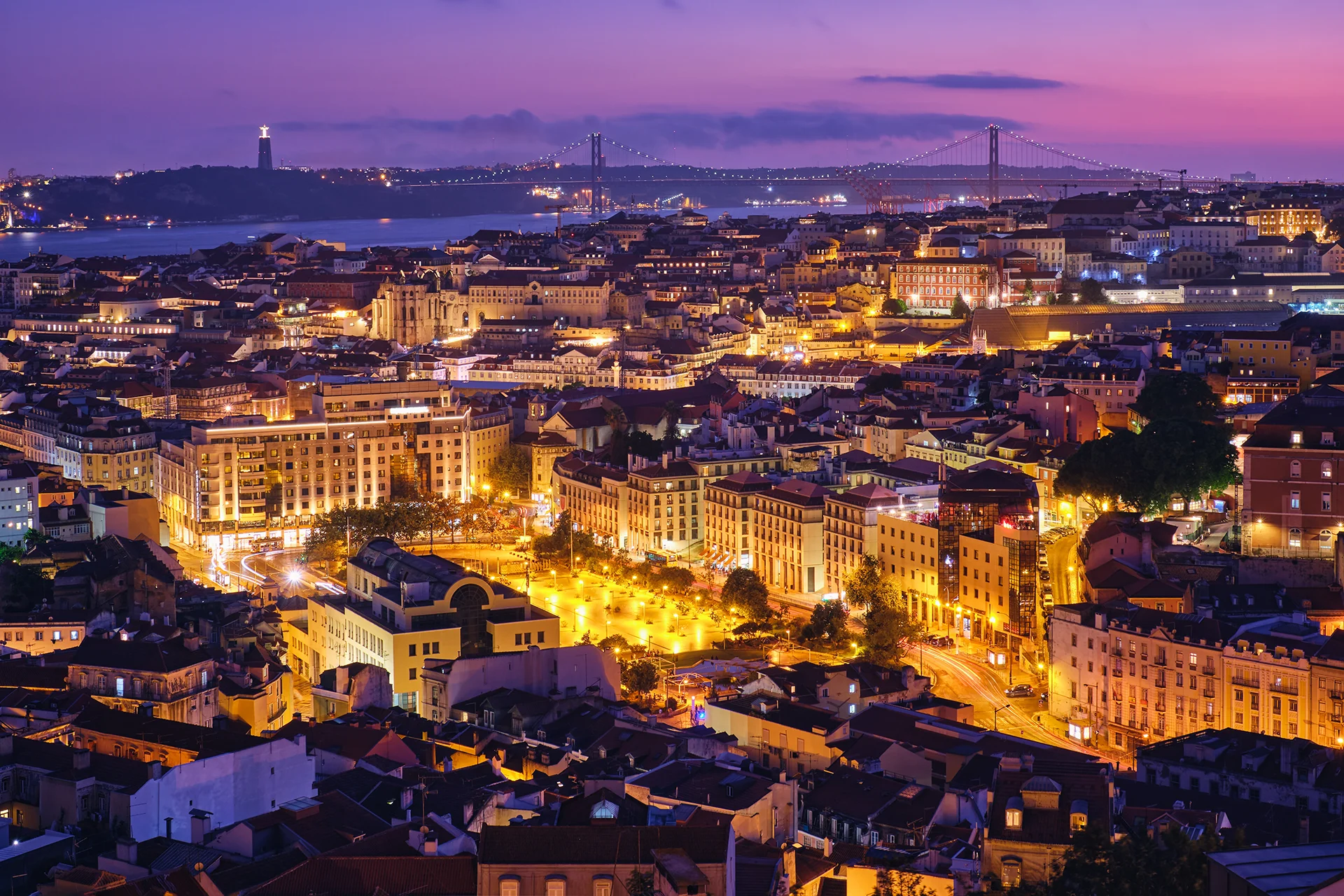 Lisbon cityscape at night with illuminated buildings, Tagus River, and 25 de Abril Bridge