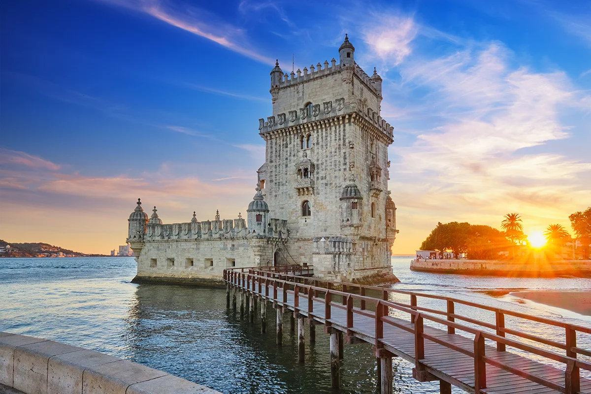 The historic Belém Tower in Lisbon at sunset with a wooden walkway across the Tagus River