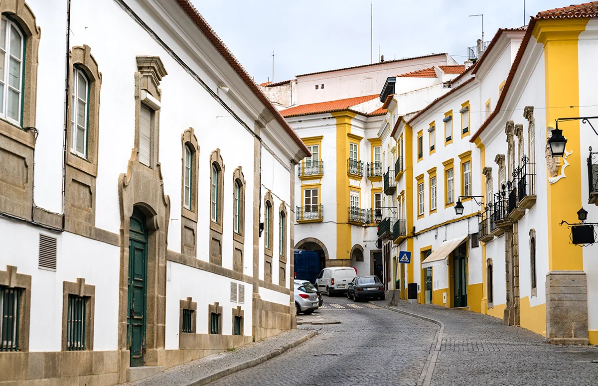 A cobblestone road curves through an old town neighborhood of yellow and white buildings