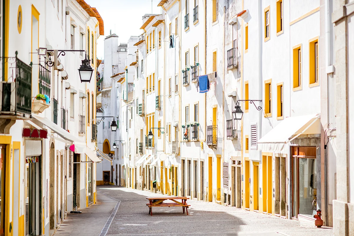 Sunlight illuminates a narrow street of traditional white houses with bright yellow trim