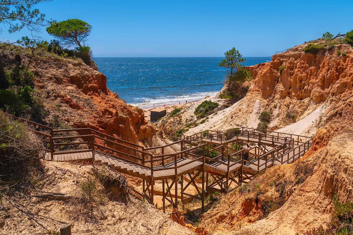 Wooden stairs weave down through rugged red ochre cliffs toward the Atlantic Ocean