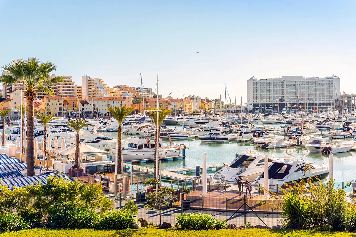 Luxury yachts dock in the sunlit Vilamoura Marina framed by tropical palm trees