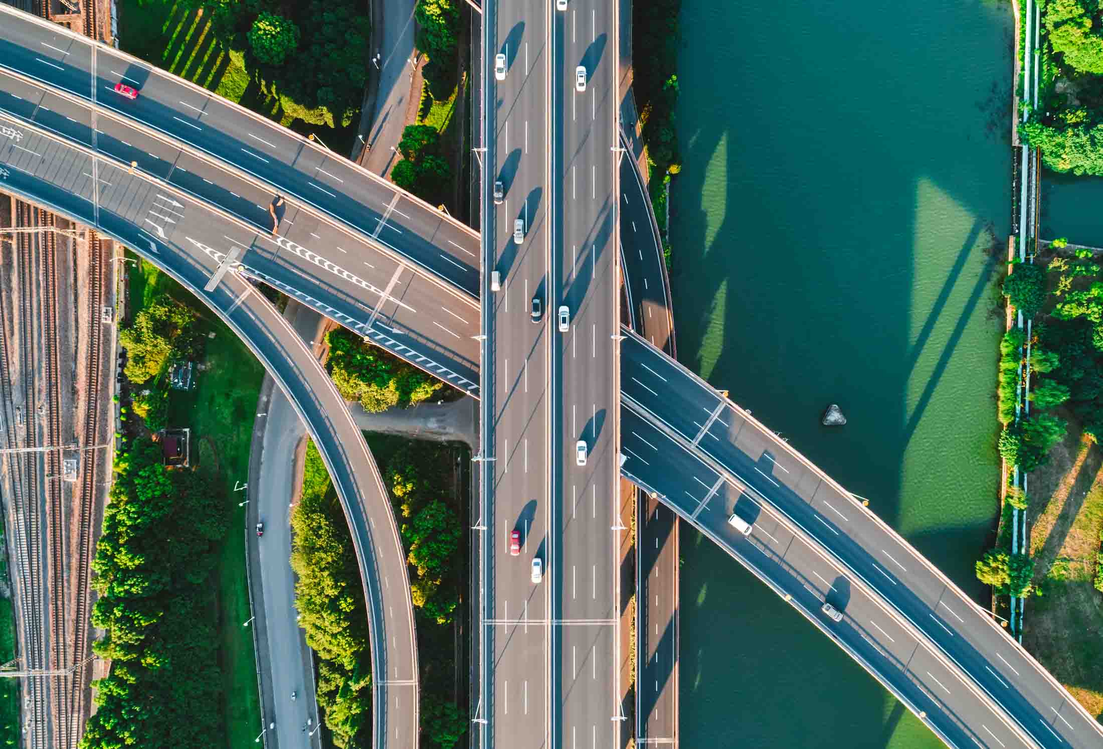 Aerial view of a multi-lane highway interchange with cars, surrounded by greenery and a body of water.
