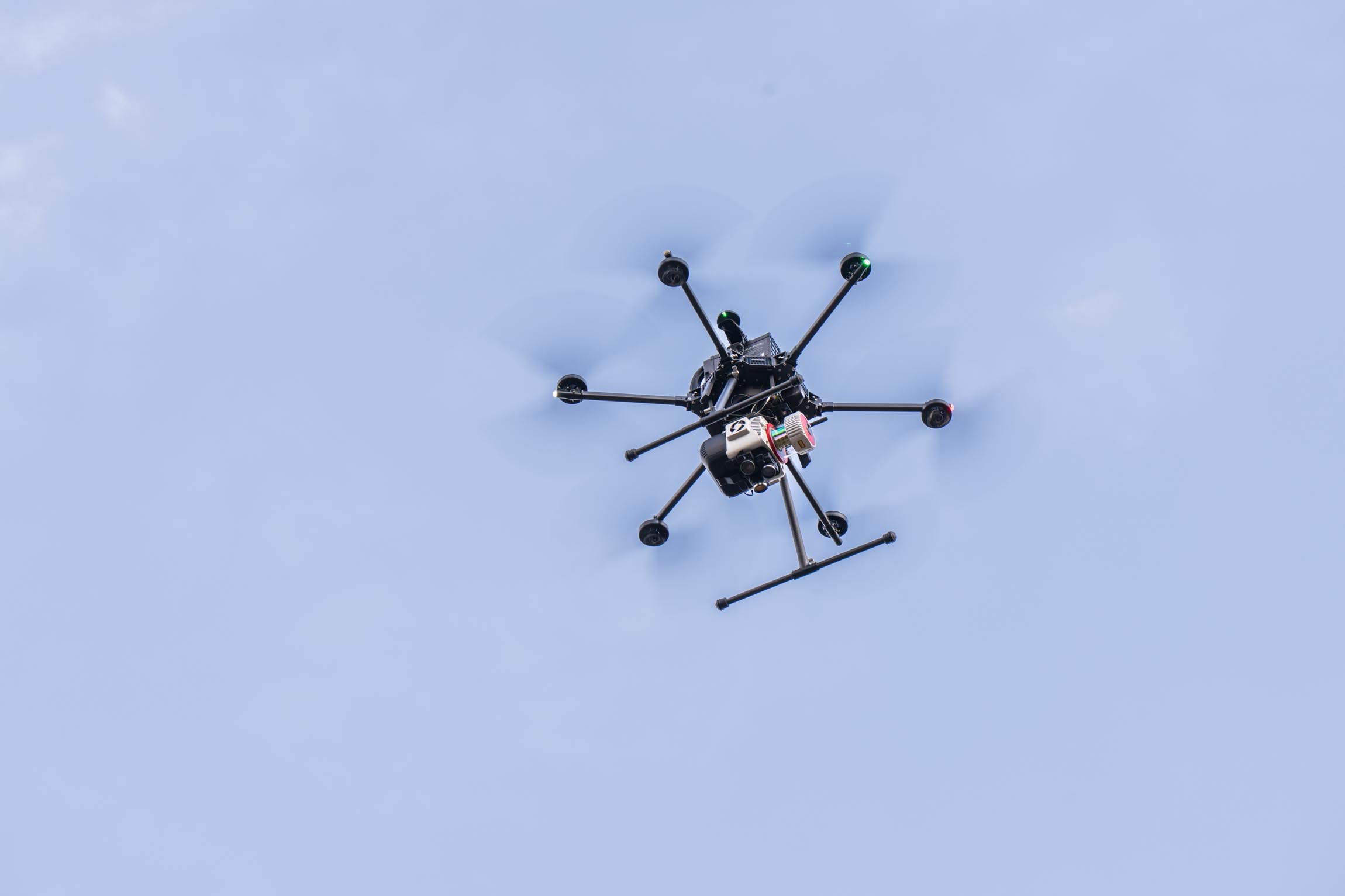 Black octocopter drone with eight propellers flying in a clear blue sky.