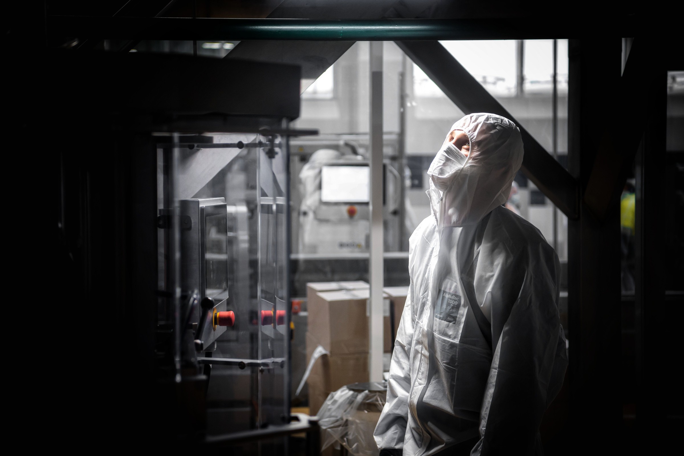 Person in protective coveralls beside equipment in a dark industrial interior.