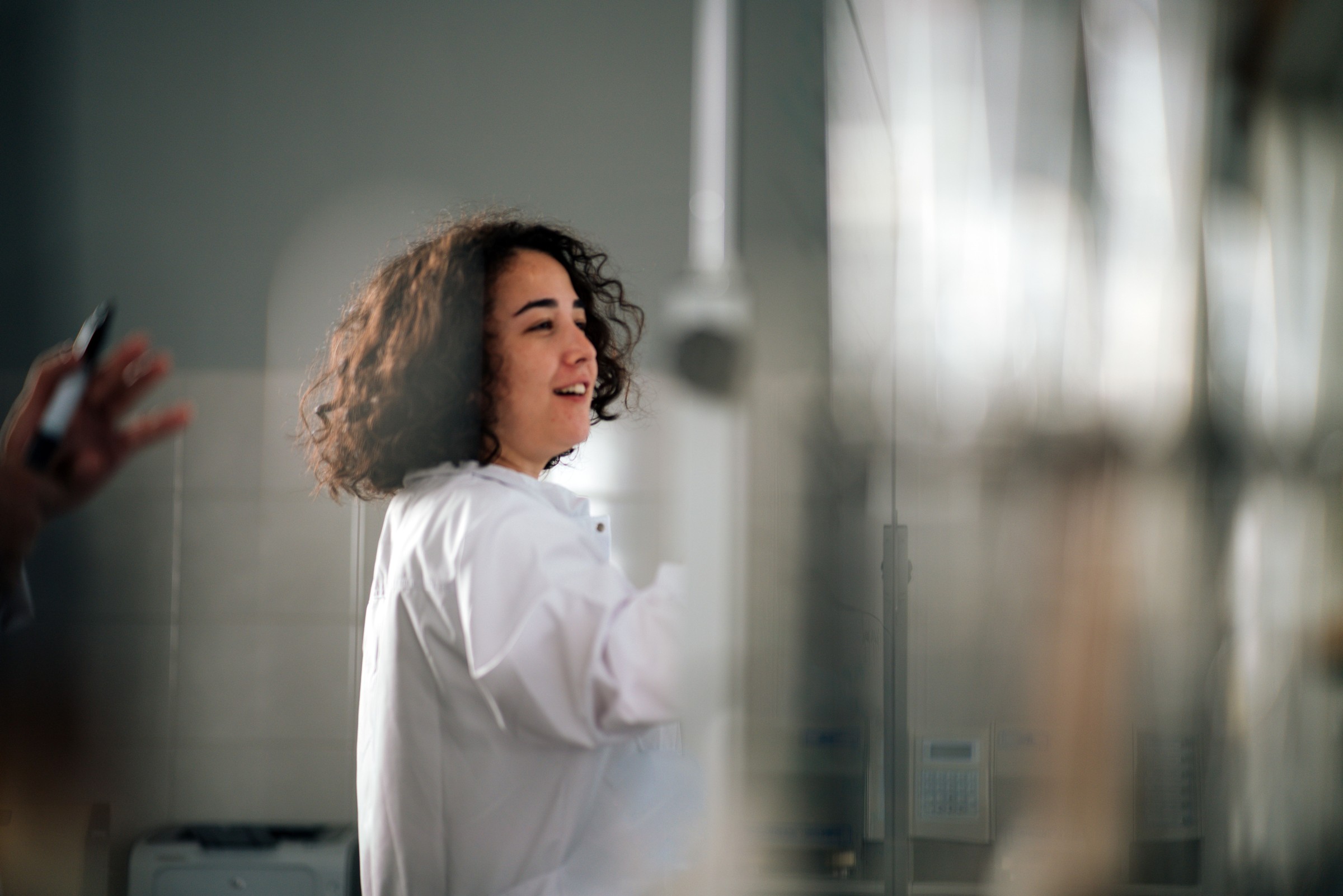 Woman in a white coat in a bright laboratory, behind a blurred foreground.