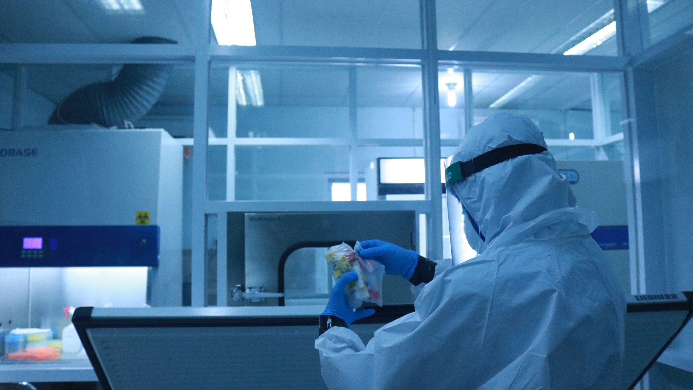Worker in protective clothing at a laboratory station lit in blue.