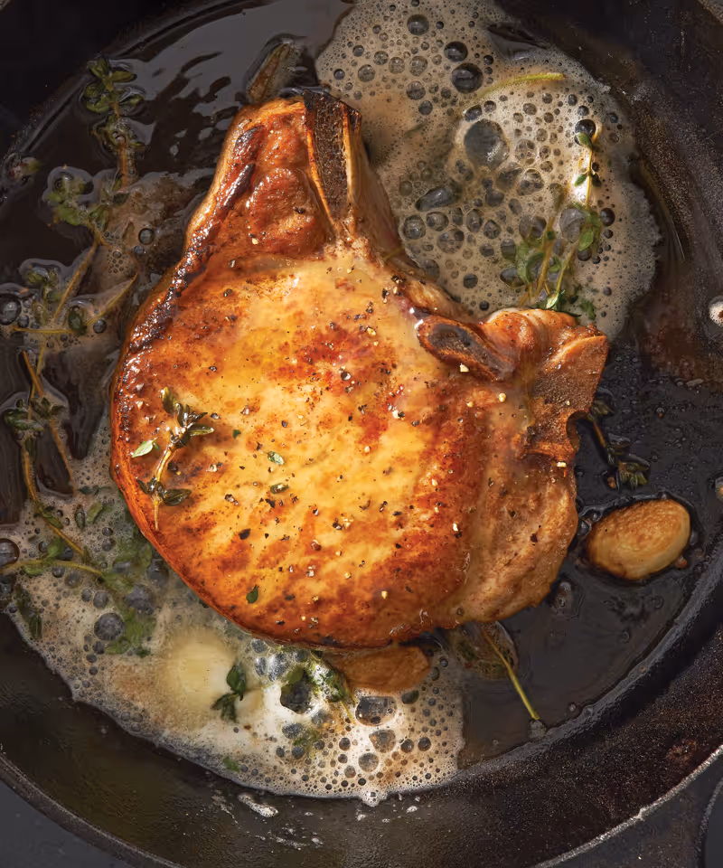 Juicy, golden-brown pork chop sizzling in a hot skillet.