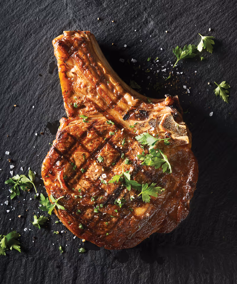 A perfectly grilled ribeye steak with rich marbling, seasoned with salt and pepper, on a dark stone counter.