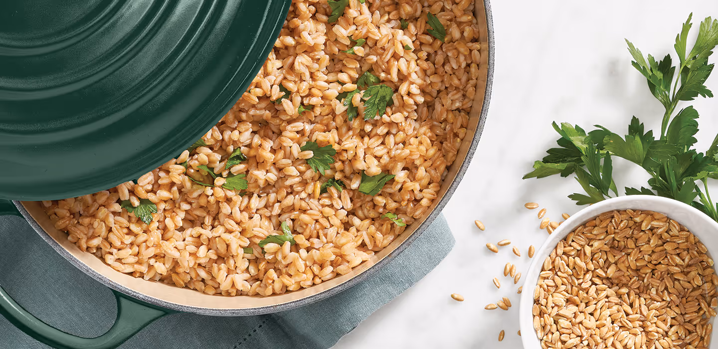 An overhead angle of a green Le Creuset Dutch oven full of cooked farro and a bowl of uncooked farro off to the side.
