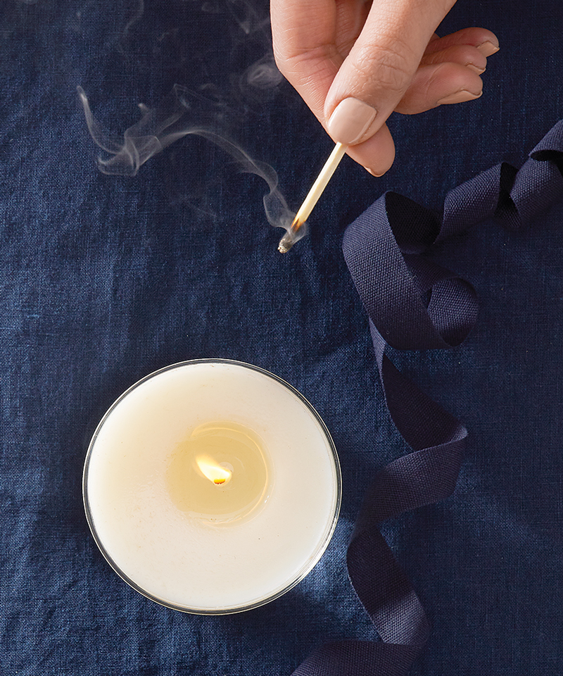 An overhead angle of a lighted candle and a hand holding a match.
