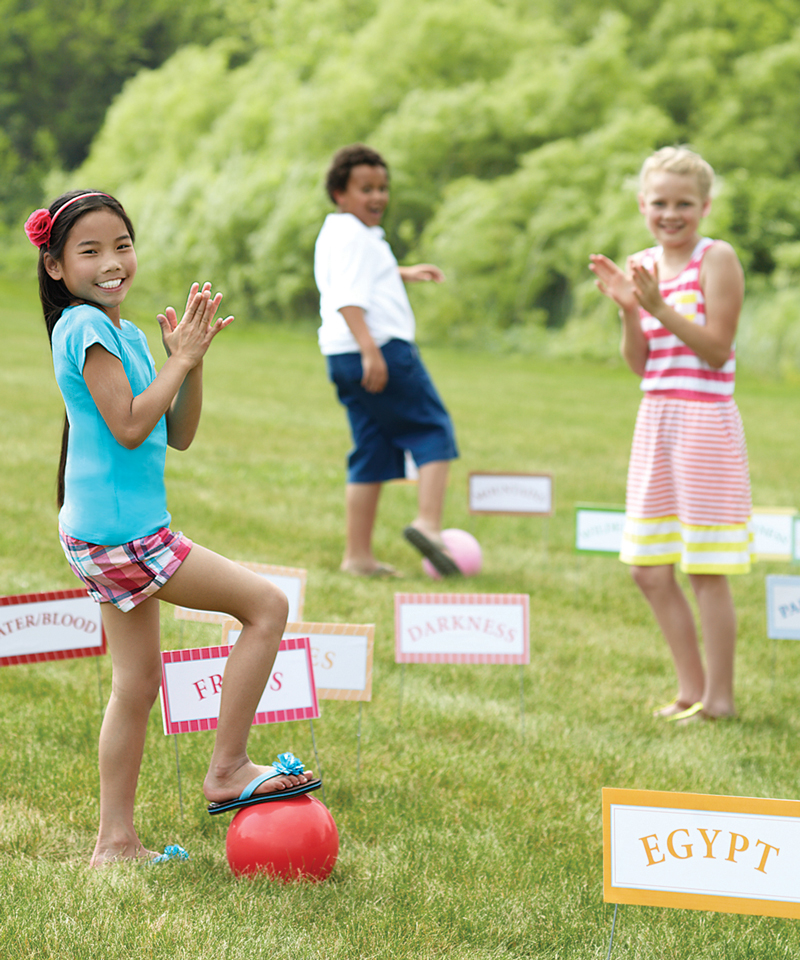 Three kids outside in a grassy yard playing a game and clapping excitedly.