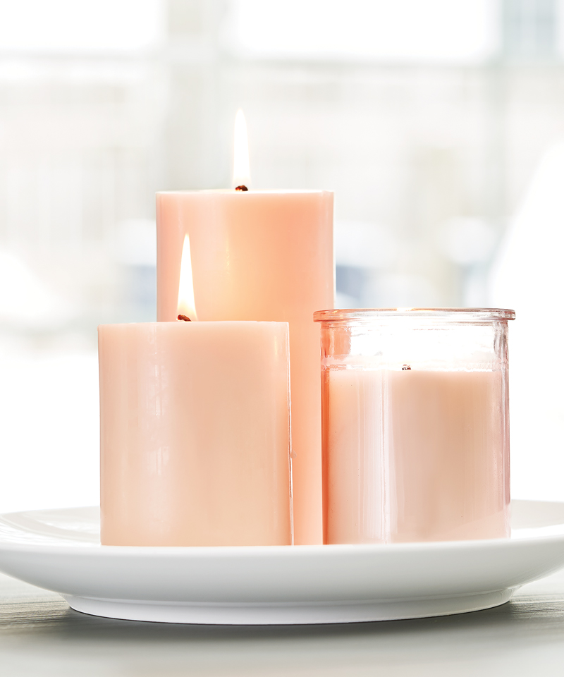 Three lighted pink candles of varying heights sitting on a white tray.