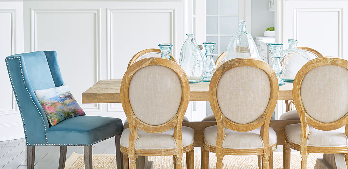 A dining room with a wood table and chairs, woven rug, chandelier, and cool-tone account décor and walls.
