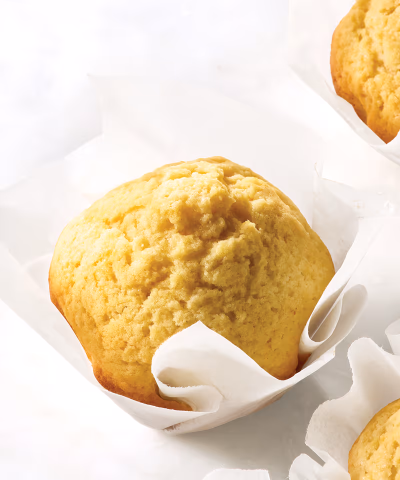 A fluffy golden cornbread muffin in parchment paper.