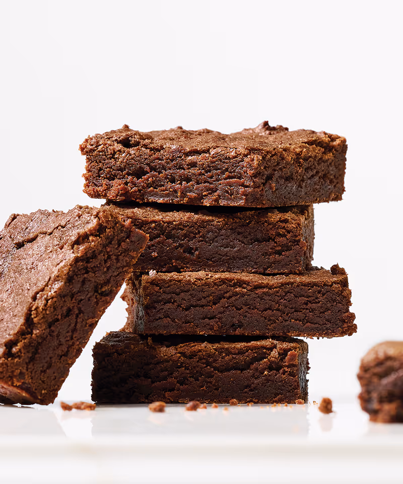 Chocolate brownie squares stacked on a surface.